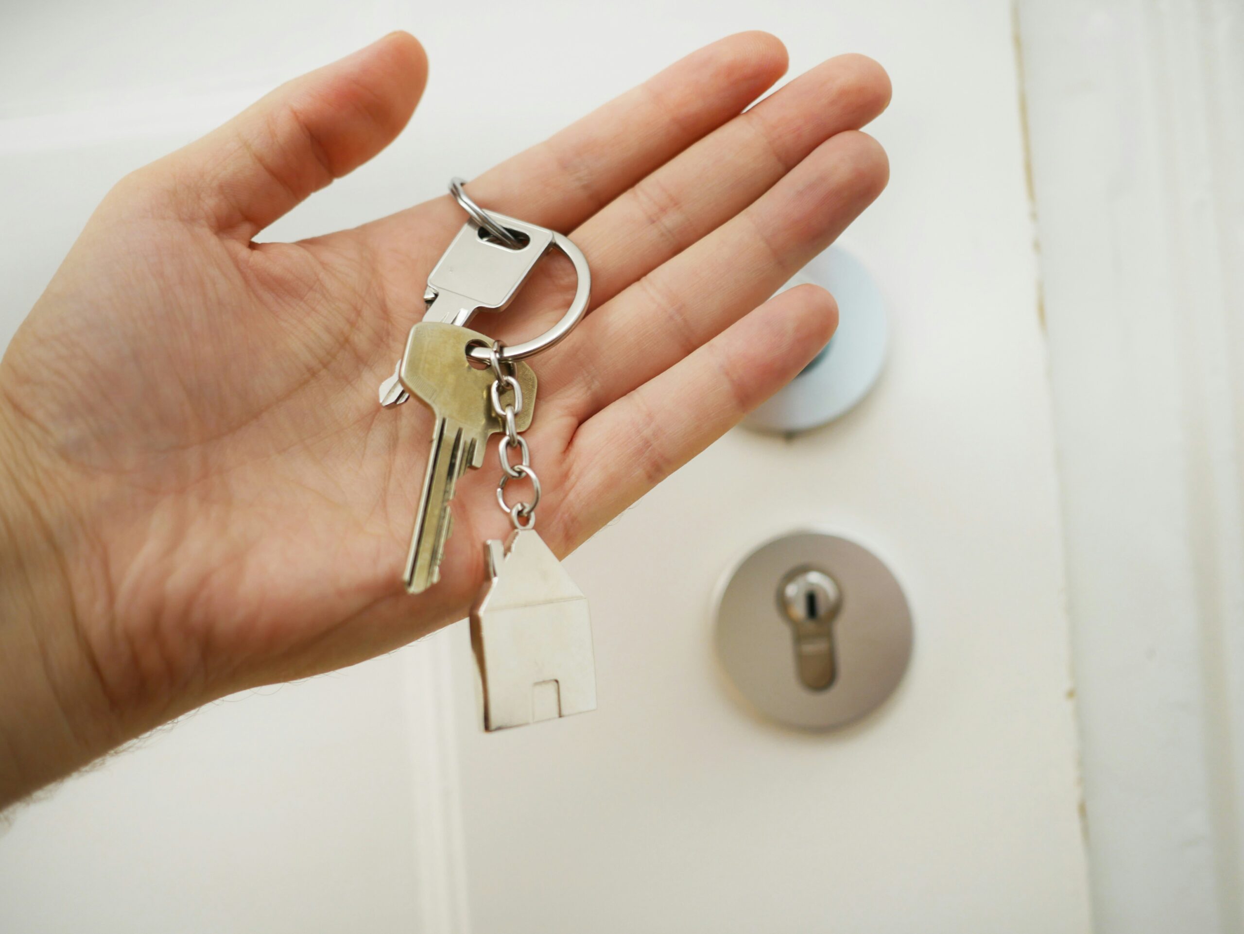 A hand holding property keys in front of a white door.