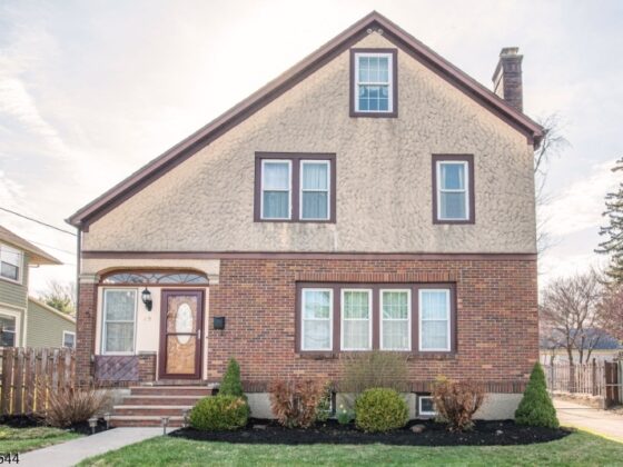 Image of a white garage door with arched windows and black hardware on a tan stone home